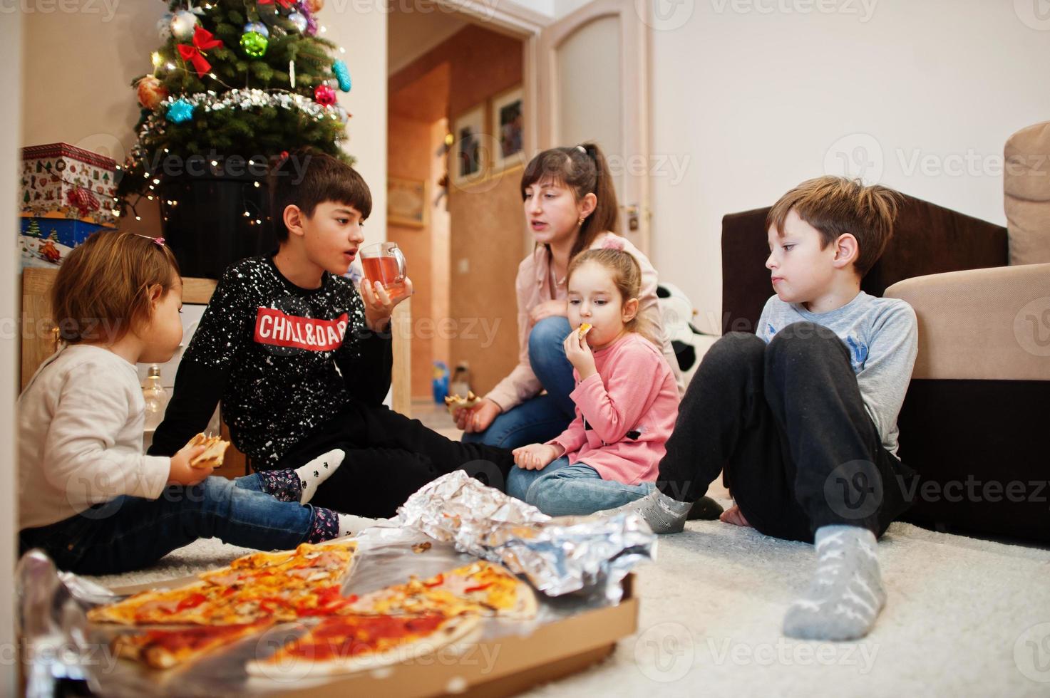 familia feliz con cuatro hijos comiendo pizza en casa. foto