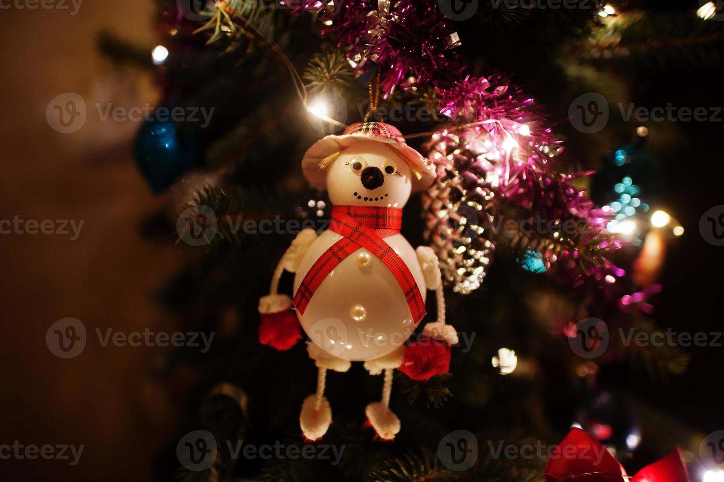 Snowman on Christmas tree with shining garlands on evening home. photo