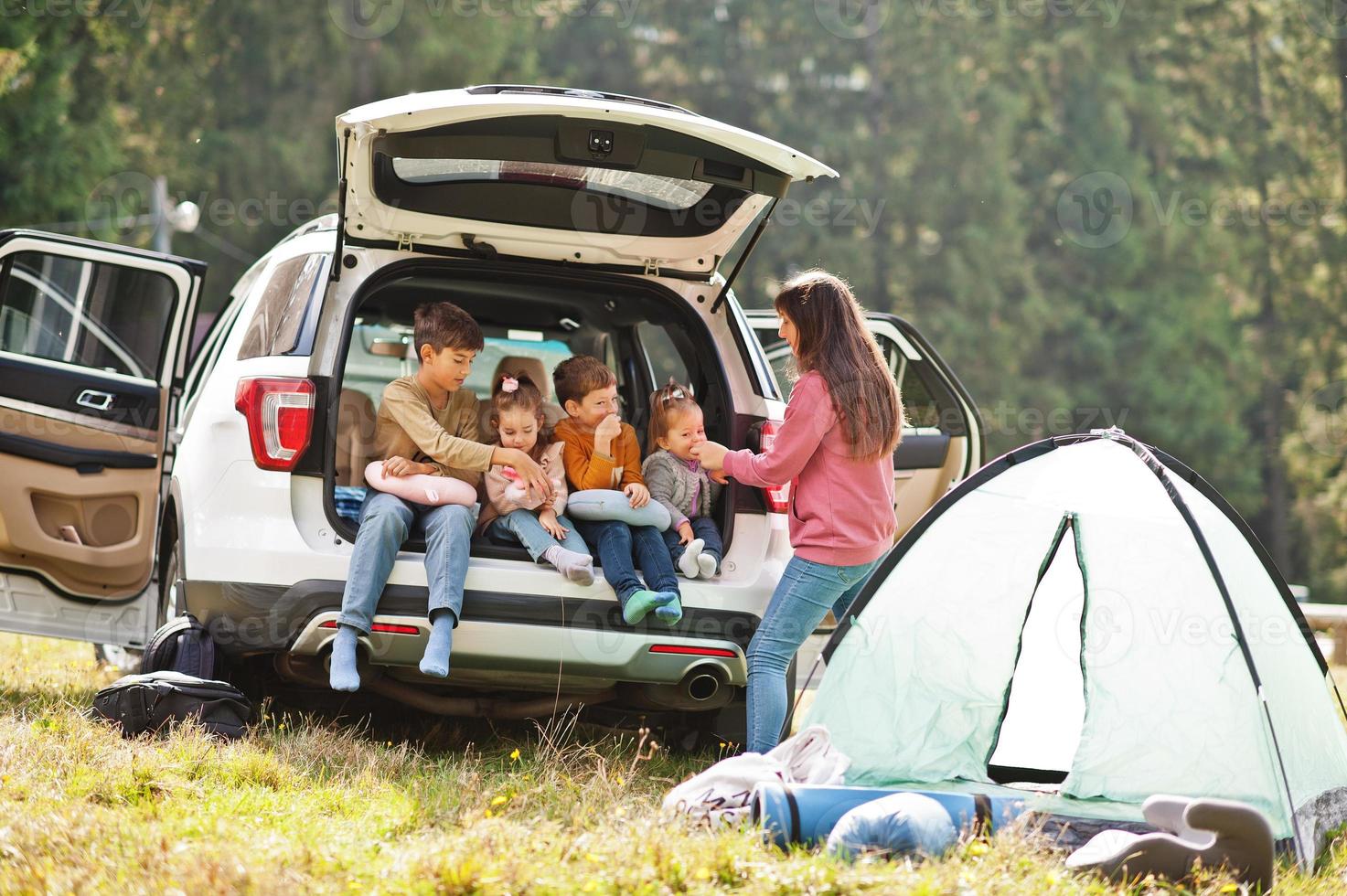 Family of four kids and mother at vehicle interior. Children sitting in trunk. Traveling by car in the mountains, atmosphere concept. photo