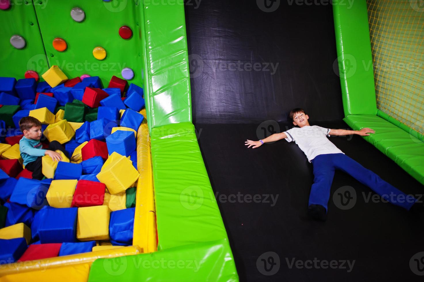 Two brothers lying on pool with colored foam cubes and trampoline in indoor play center. photo