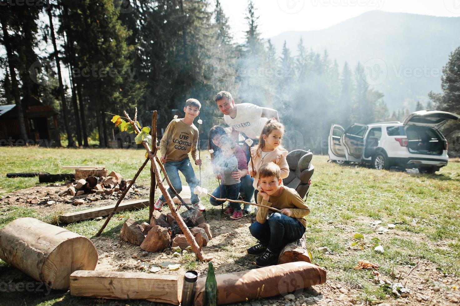 Family bonfire in mountain.Four kids camping. Bbq marshmallow. Autumn hike and camp weather. Warming and cooking near flame together. photo