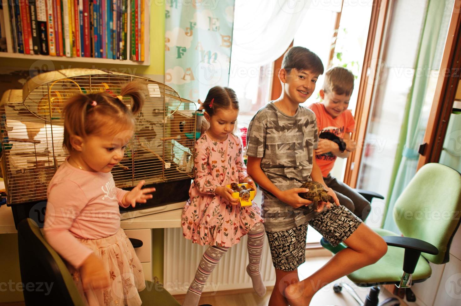 Four children holding their favorite pets on hands. Kids playing with hamster,turtle and parrots at home. photo