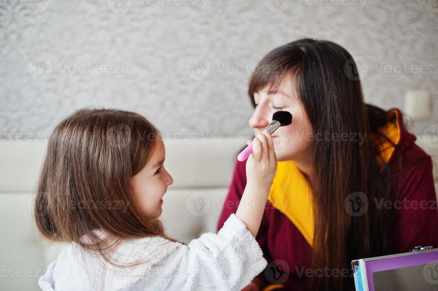 Mother and daughter doing makeup on the bed in the bedroom. photo