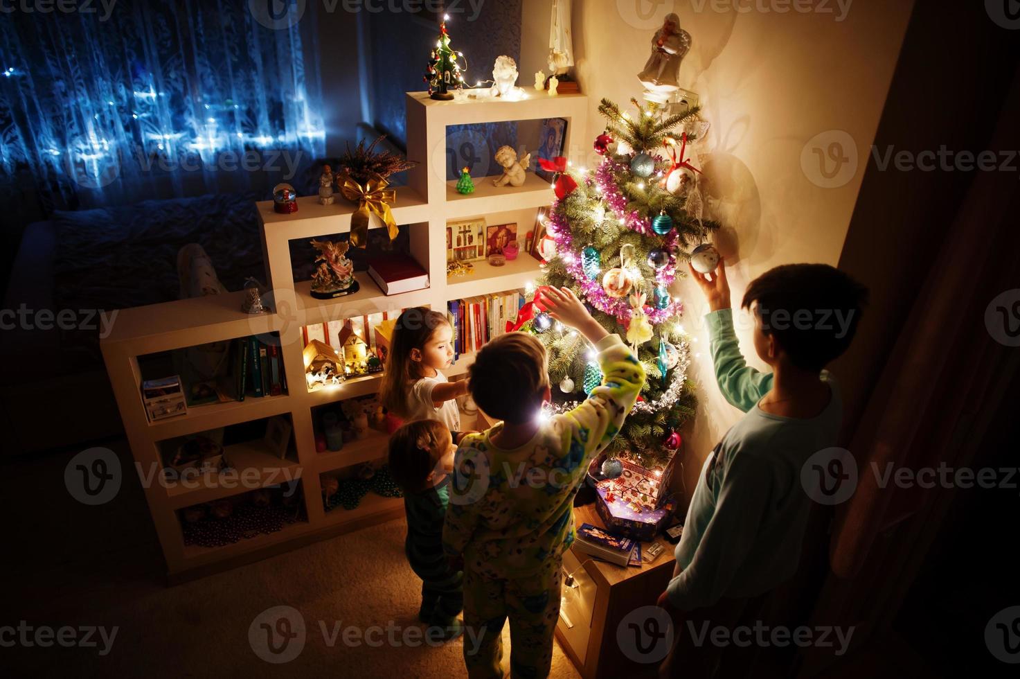 Kids looking on Christmas tree with shining garlands on evening home. photo