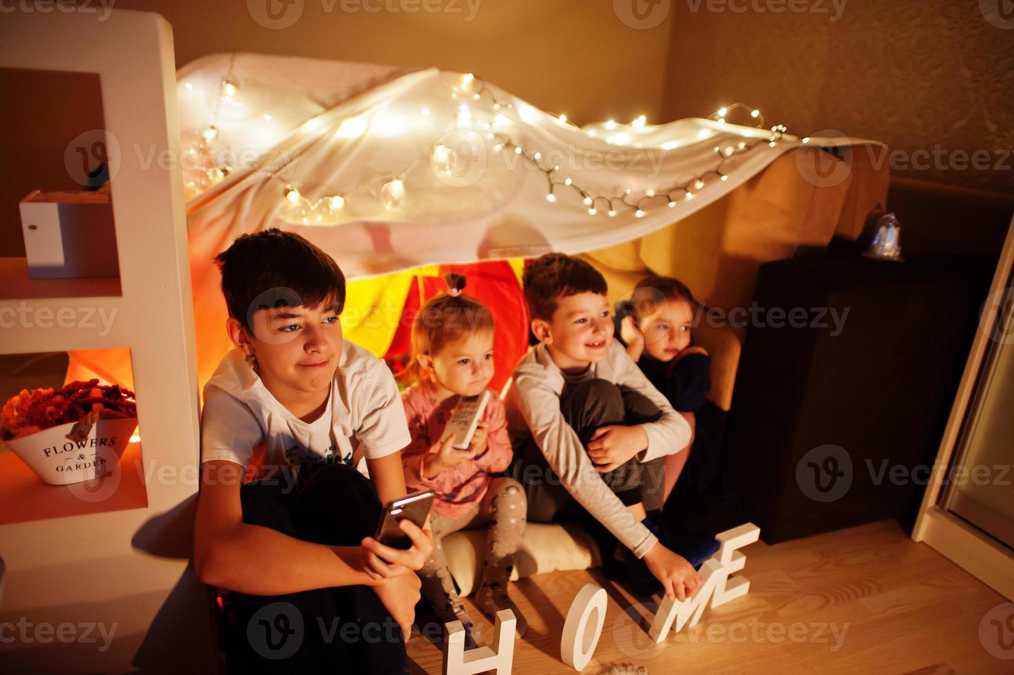 Kids in tent waching tv at night home. Hygge mood. photo