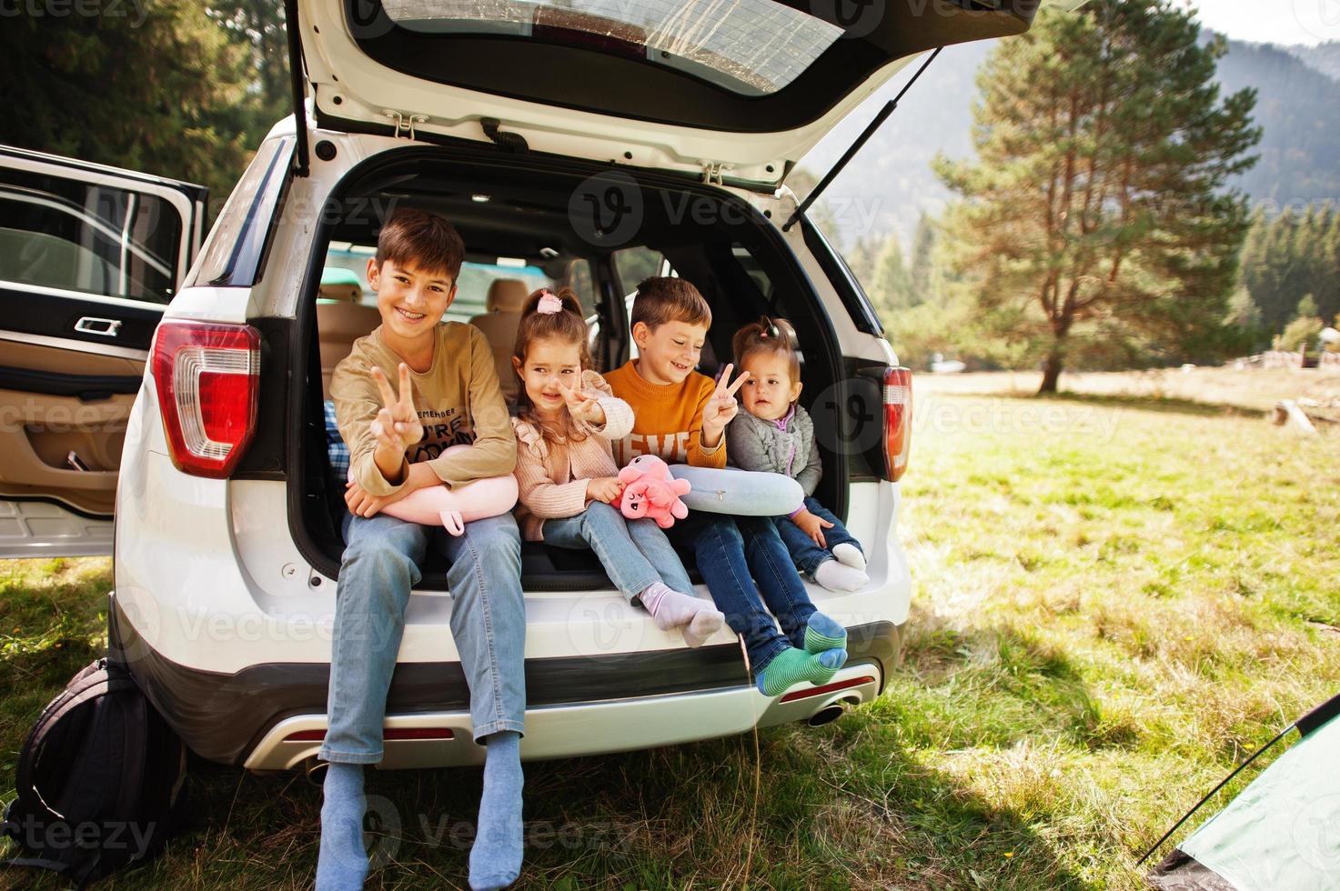 familia de cuatro hijos en el interior del vehículo. niños sentados en el baúl. viajar en coche por las montañas, concepto de ambiente. foto