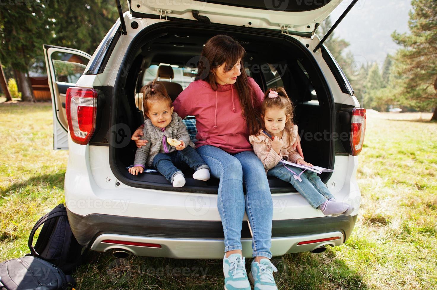 Family at vehicle interior. Mother with her daughters. Children in trunk. Traveling by car in the mountains, atmosphere concept. photo