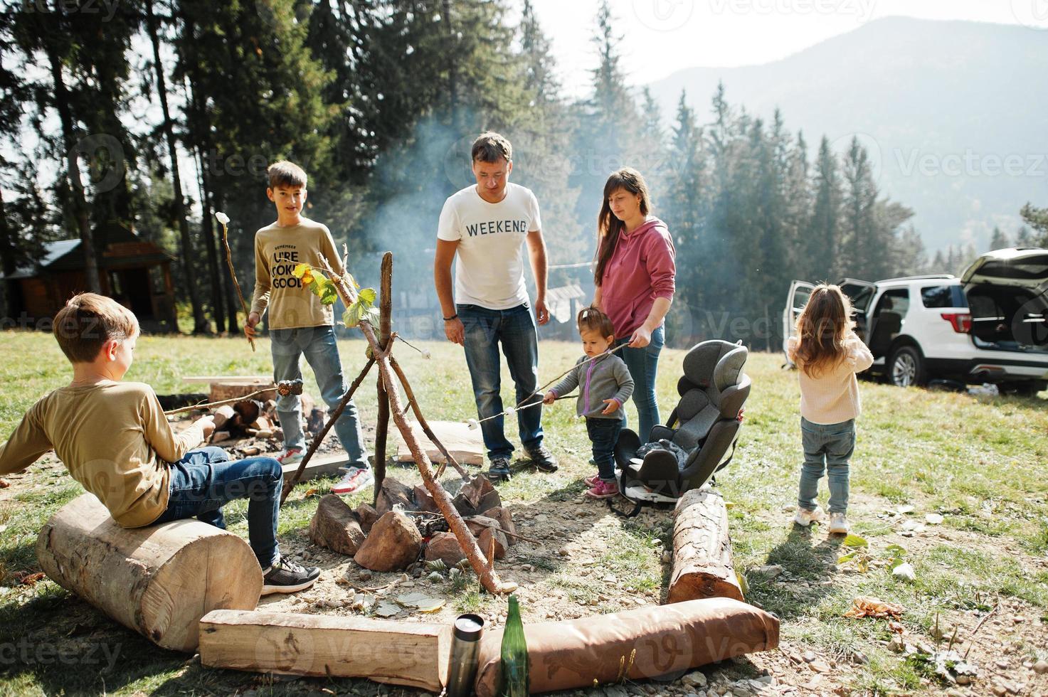 Family bonfire in mountain.Four kids camping. Bbq marshmallow. Autumn hike and camp weather. Warming and cooking near flame together. photo