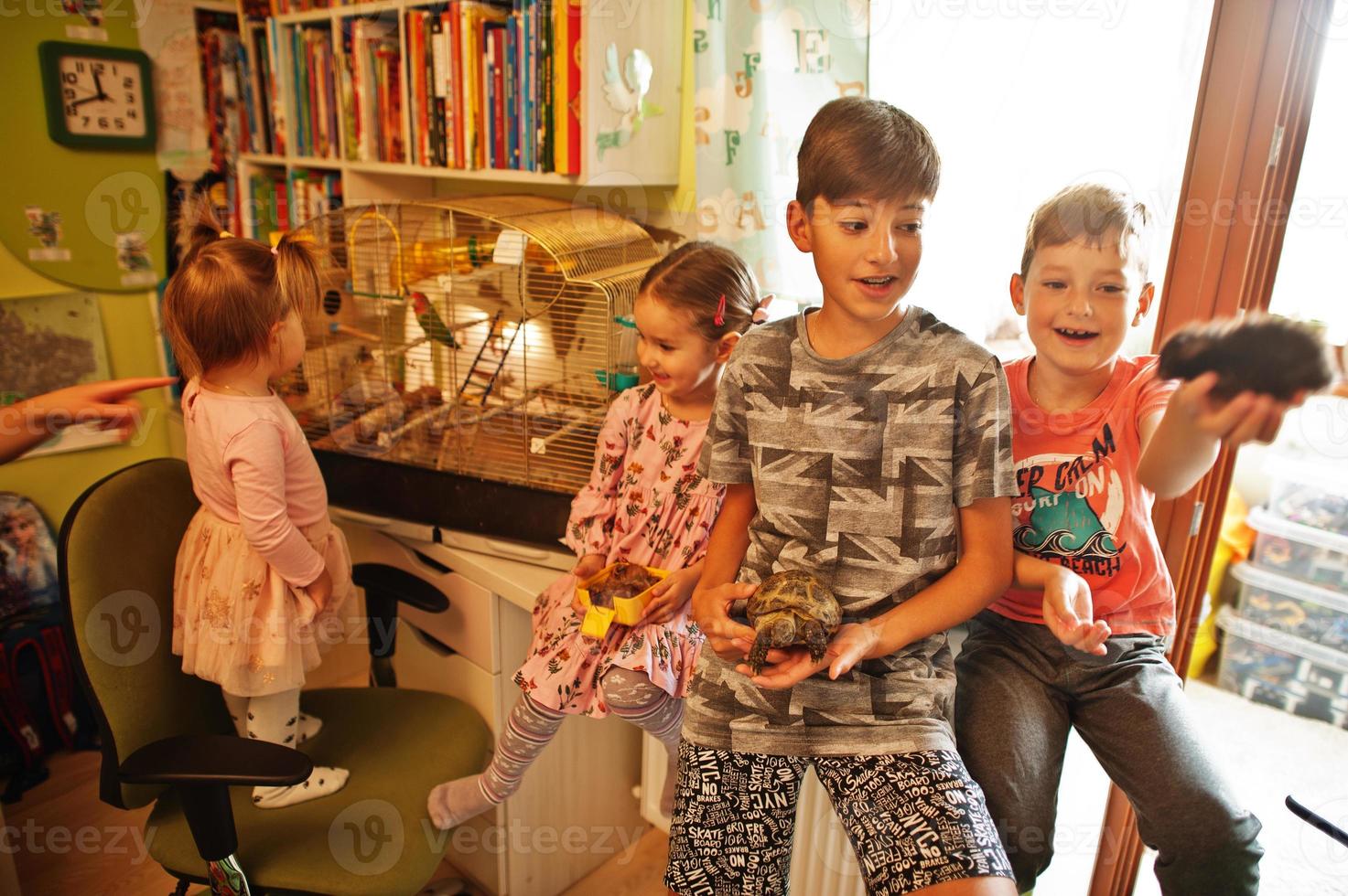 Four children holding their favorite pets on hands. Kids playing with hamster,turtle and parrots at home. photo