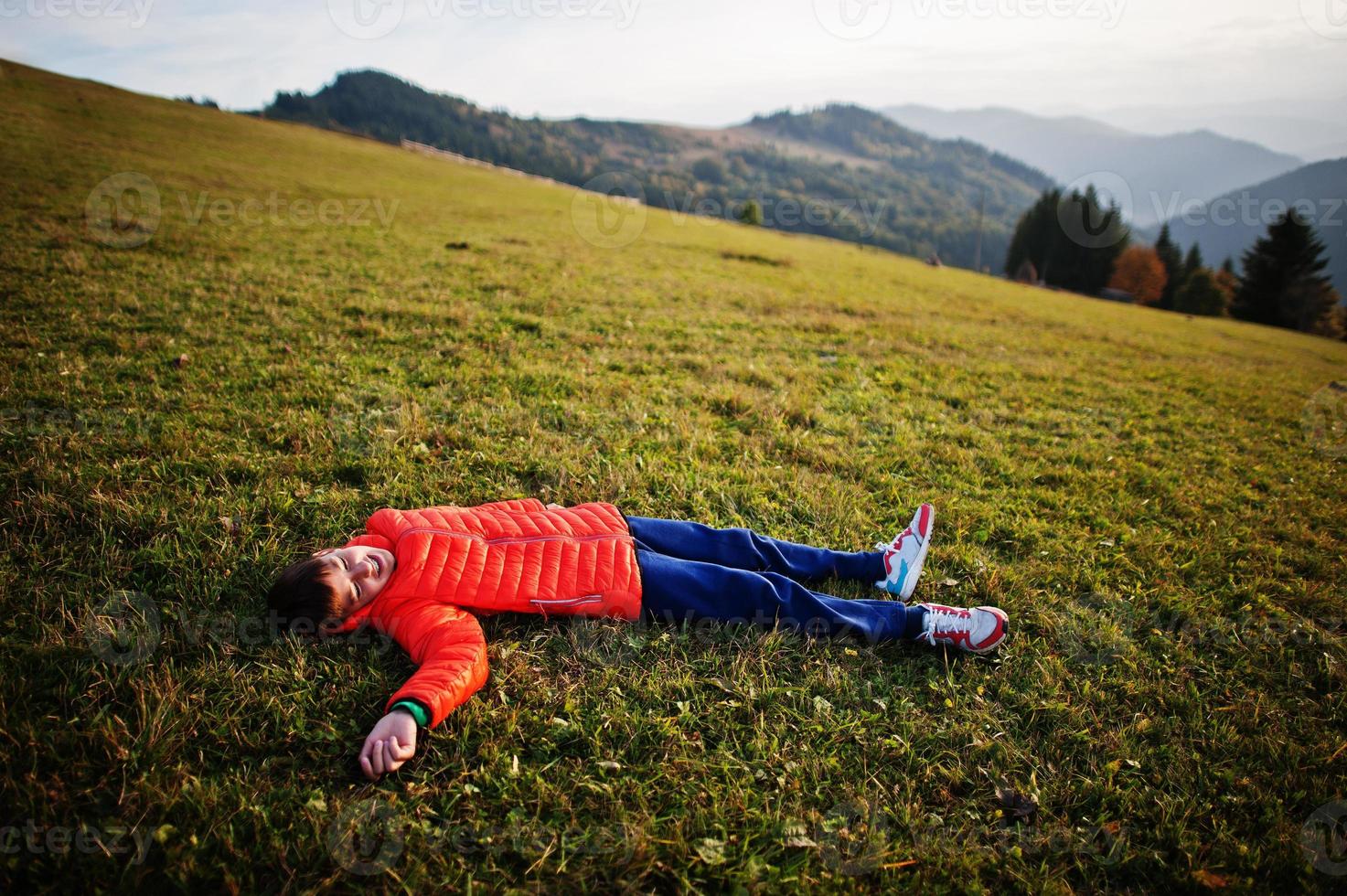 Boy lying in the grass with a gorgeous mountain range in the horizon. photo