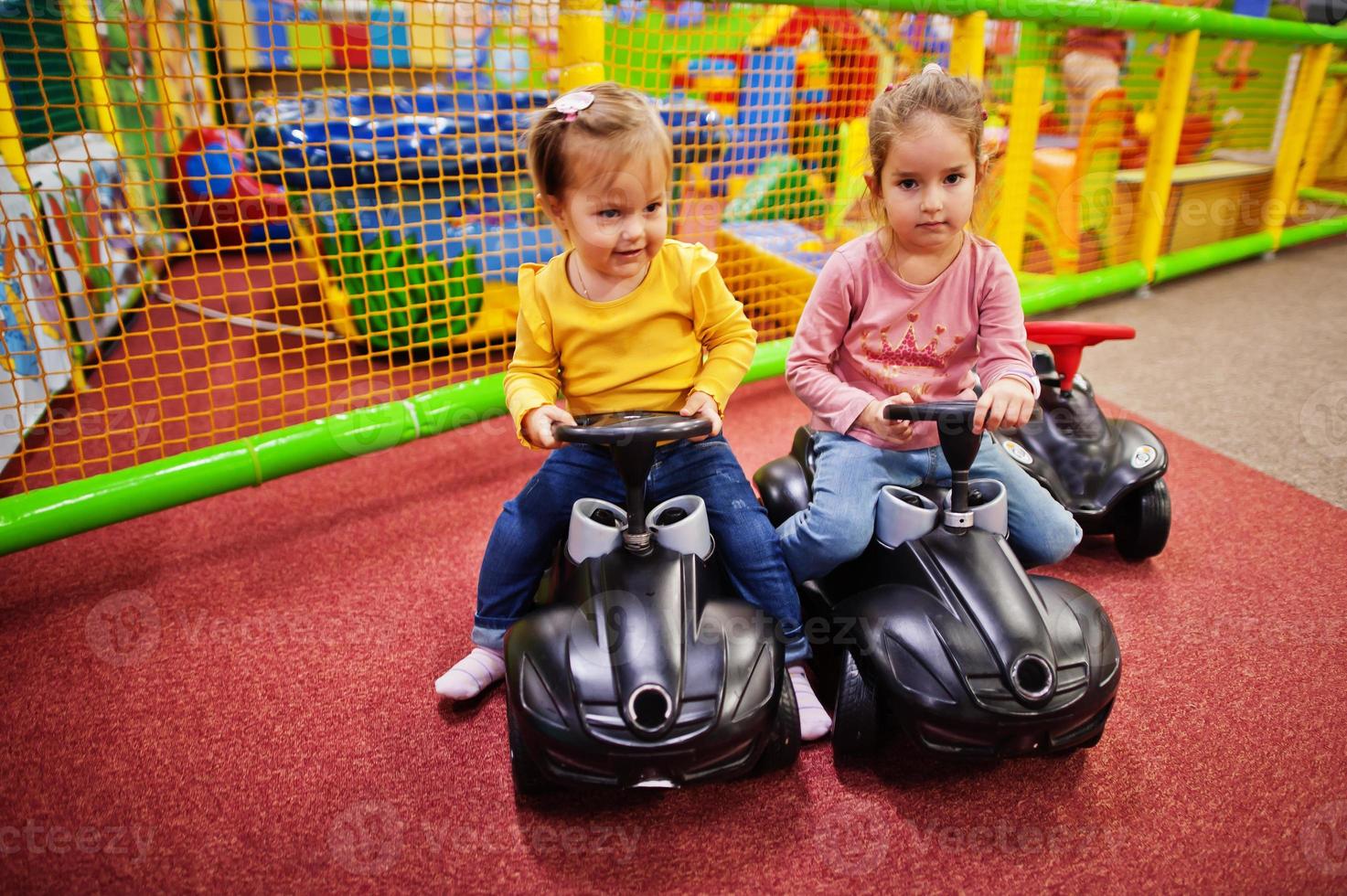 Two siters rides on a plastic cars in indoor play center. photo