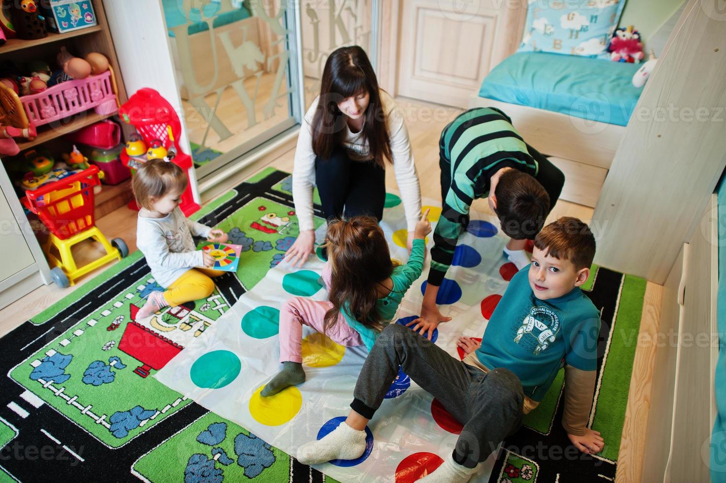 Happy family having fun together,four kids and mother playing twister game at home. photo