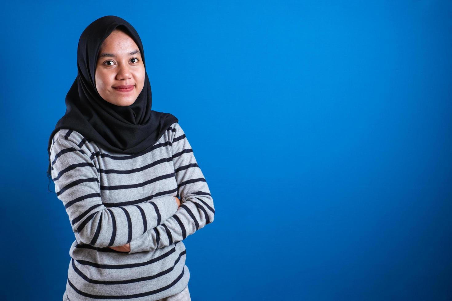 Asian muslim college student girl wearing hijab smiling friendly with arms crossed photo