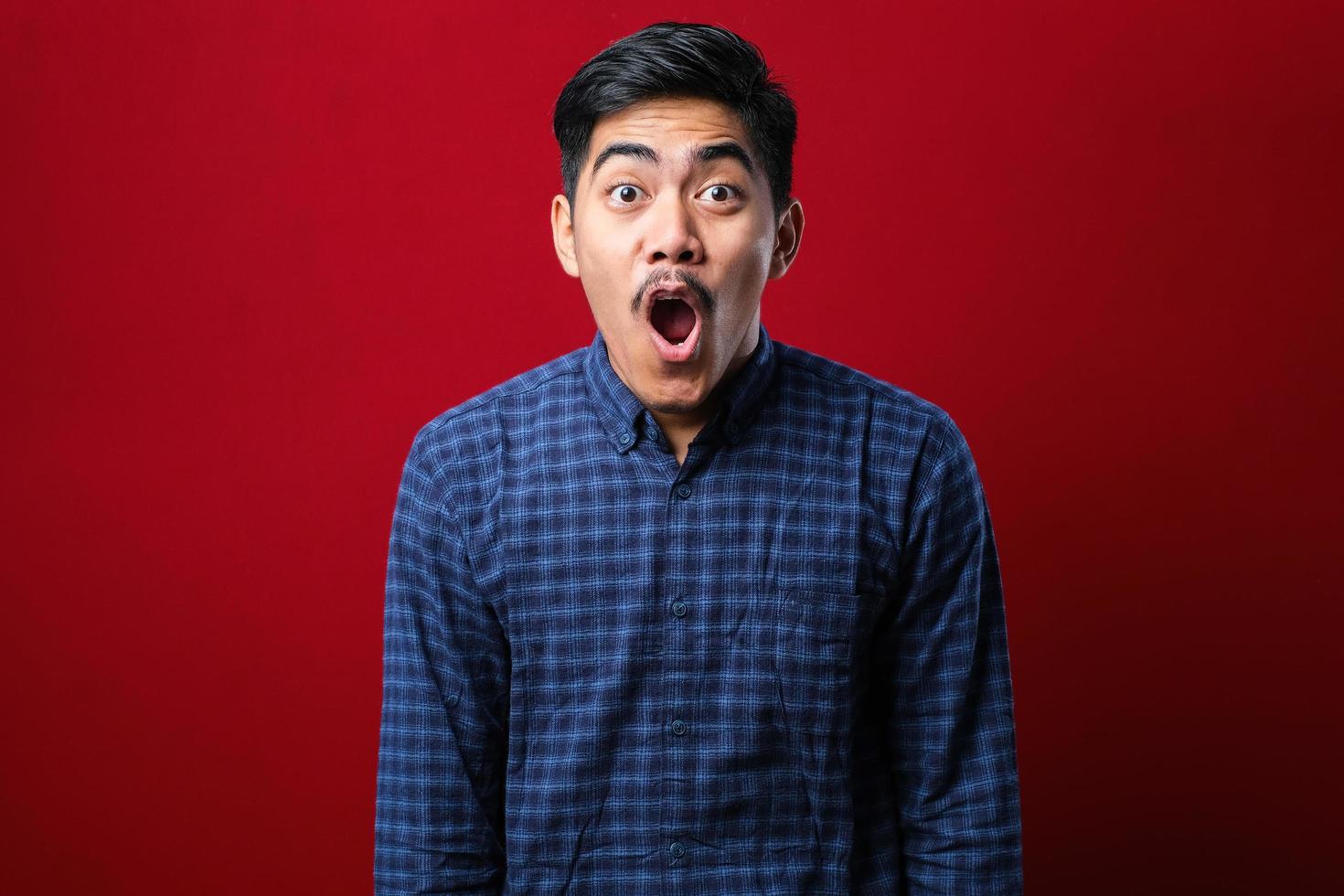 Amazed asian young man with open mouth and bulging eyes looking at camera photo