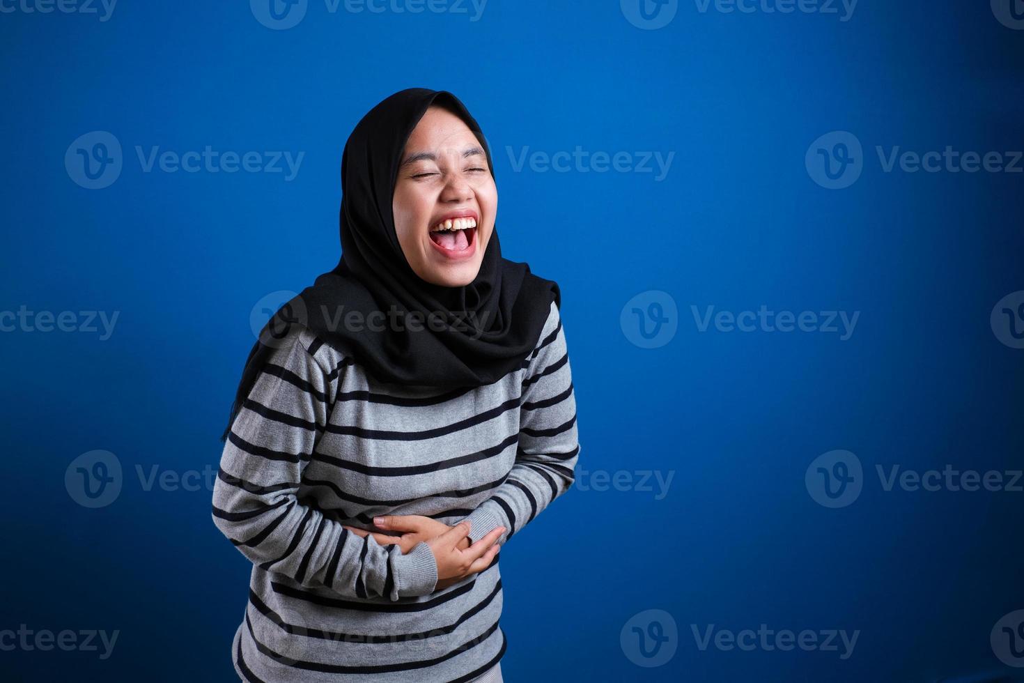 muslim woman laughing hard while holding her belly, happy excited expression photo