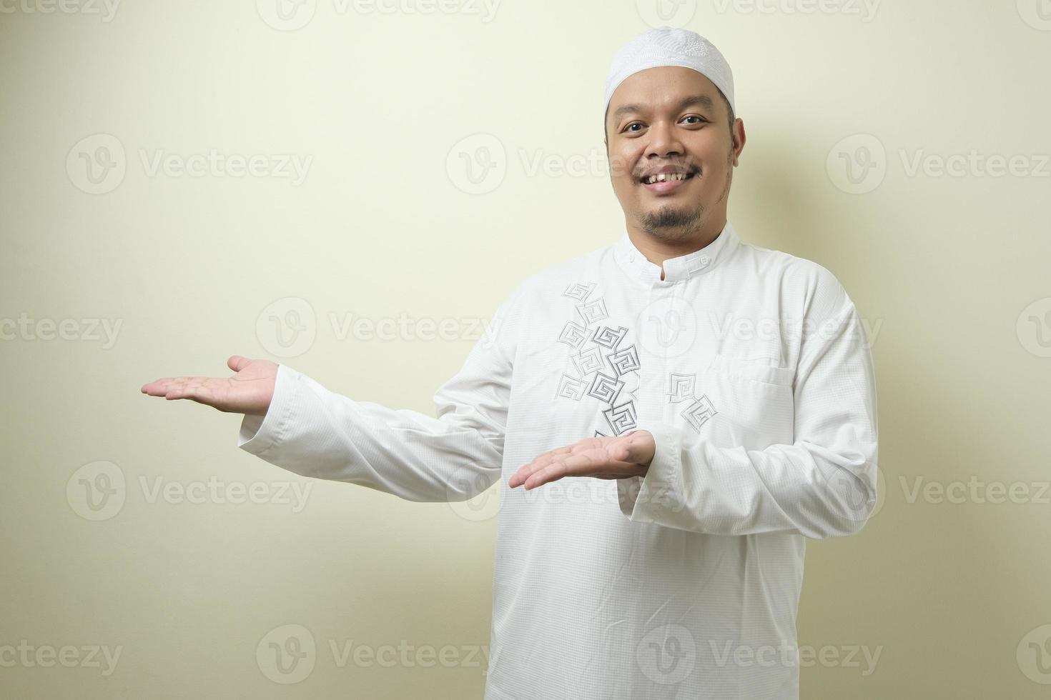 Portrait of Asian young muslim man smiling and pointing to presenting something on his side photo