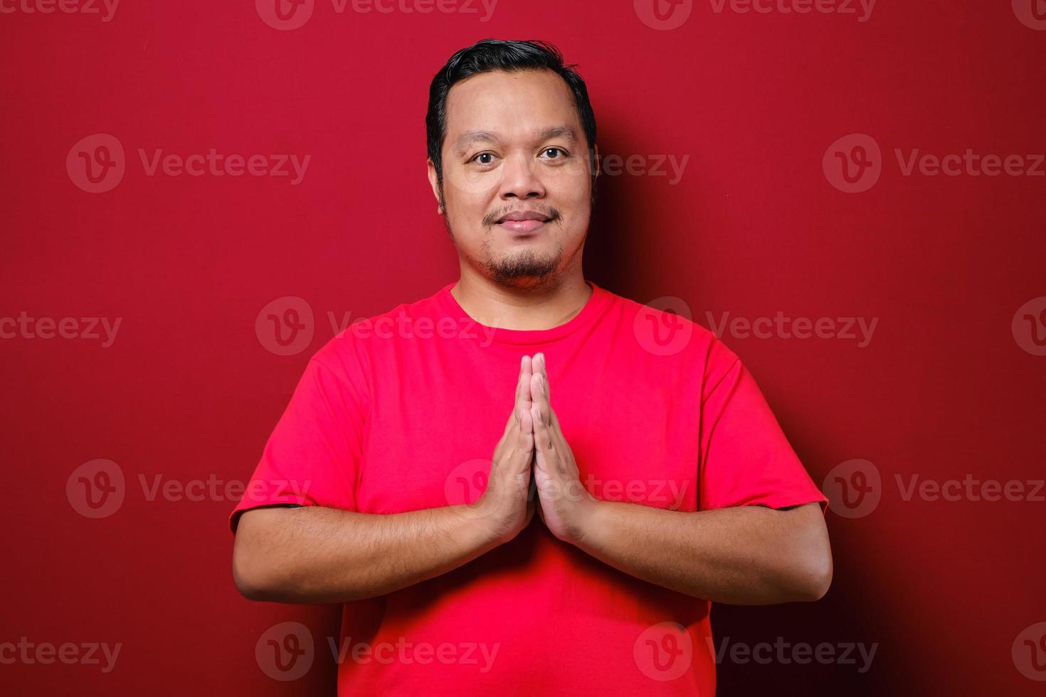 Young Asian man wearing red t-shirt with greeting and welcoming gesture photo