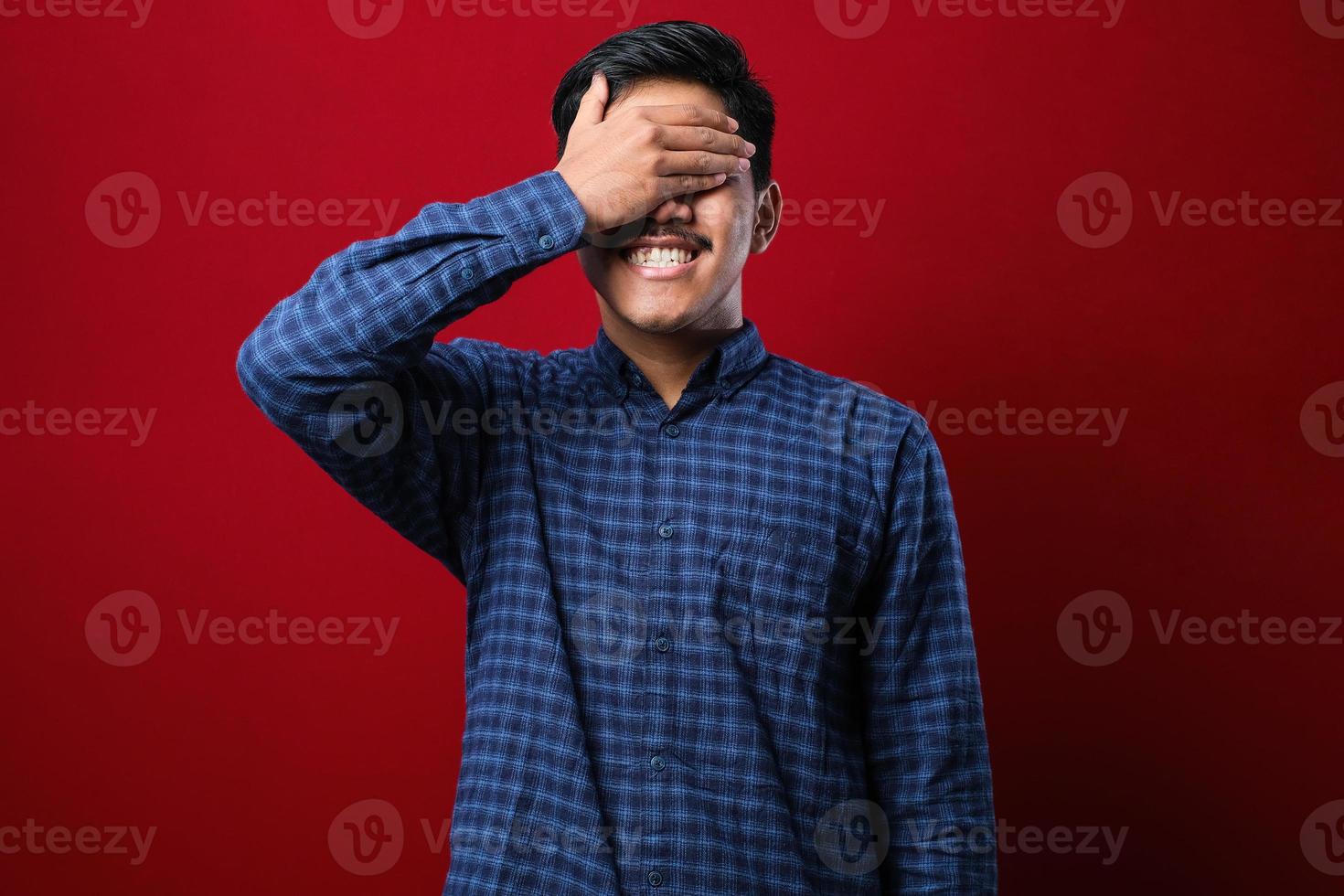 joven pelirrojo con camisa casual sonriendo y riendo con la mano en la cara cubriendo los ojos por sorpresa foto