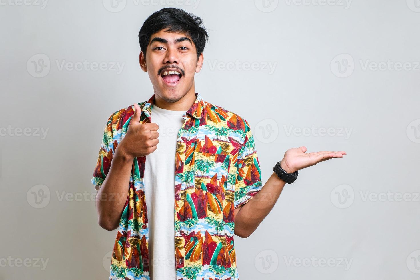 Asian man in white tshirt smiling and pointing to presenting something on his side, against red background with copy space photo