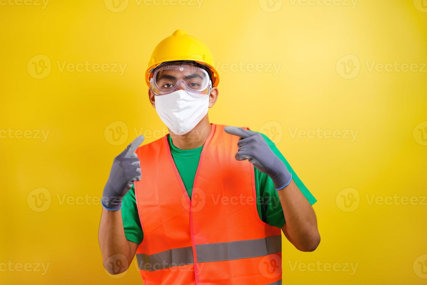 trabajador de la construcción asiático señalando su máscara protectora y su casco de seguridad foto