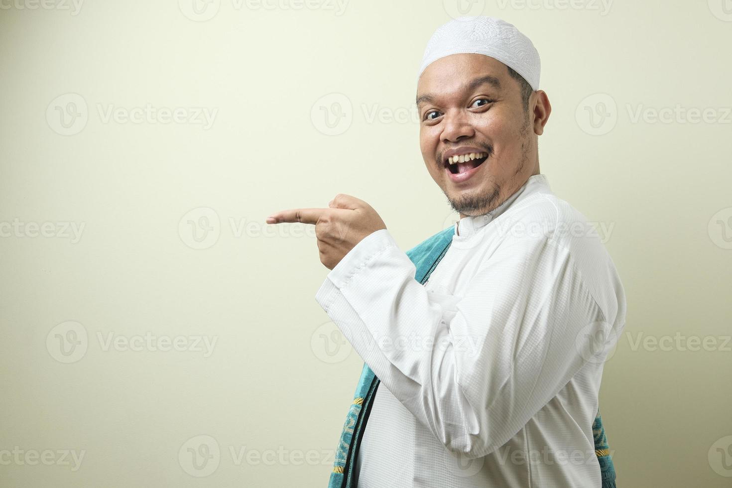 Portrait of Asian young muslim man smiling and pointing to presenting something on his side photo