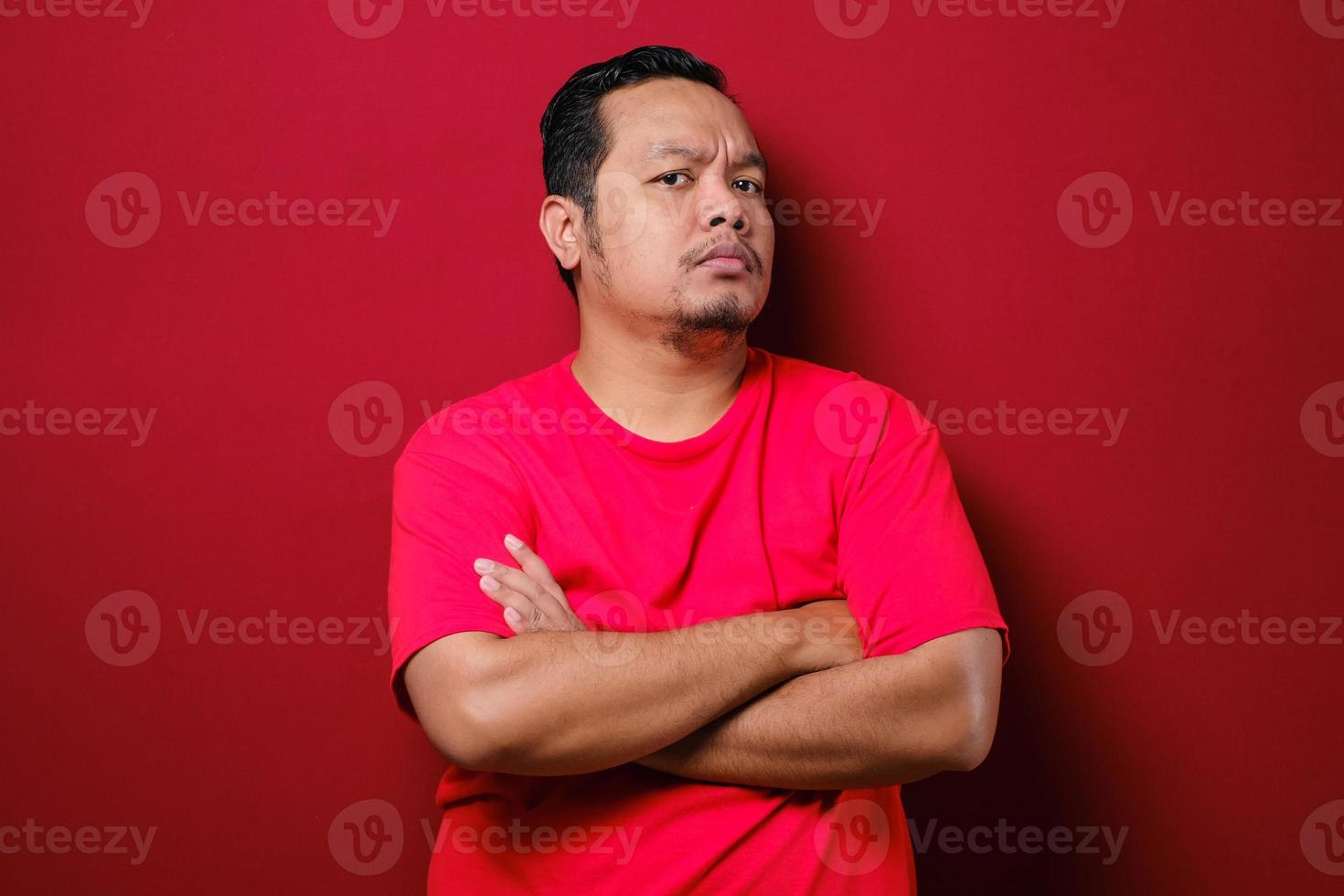 Portrait of young Asian man staring at camera with suspicious cynical expression, arms crossed on chest photo