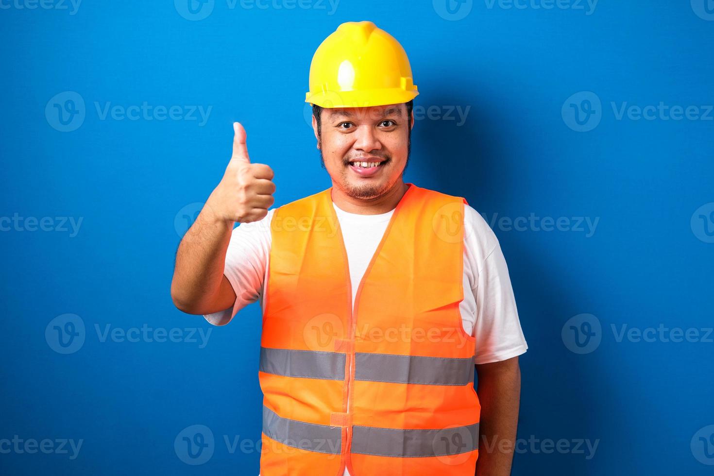 Fat asian construction worker wearing orange safety vest and helmet showing thumb up sign photo