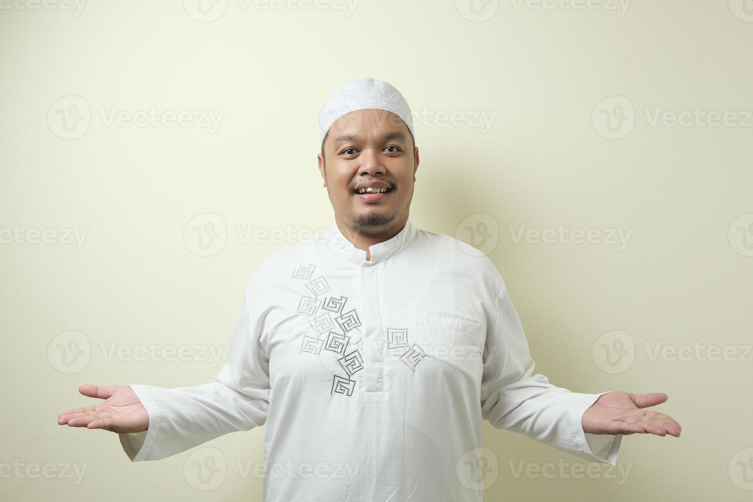 Portrait of Asian young muslim man smiling and pointing to presenting something on his side photo