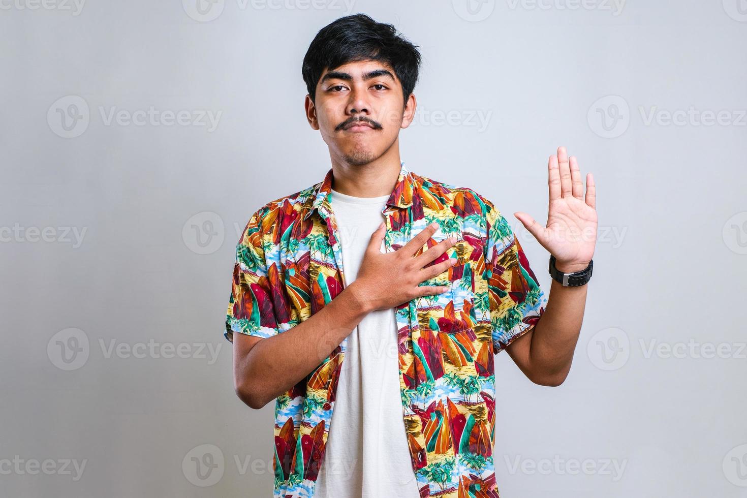 Asian man smiling swearing with hand on chest and fingers up, making a loyalty promise oath photo