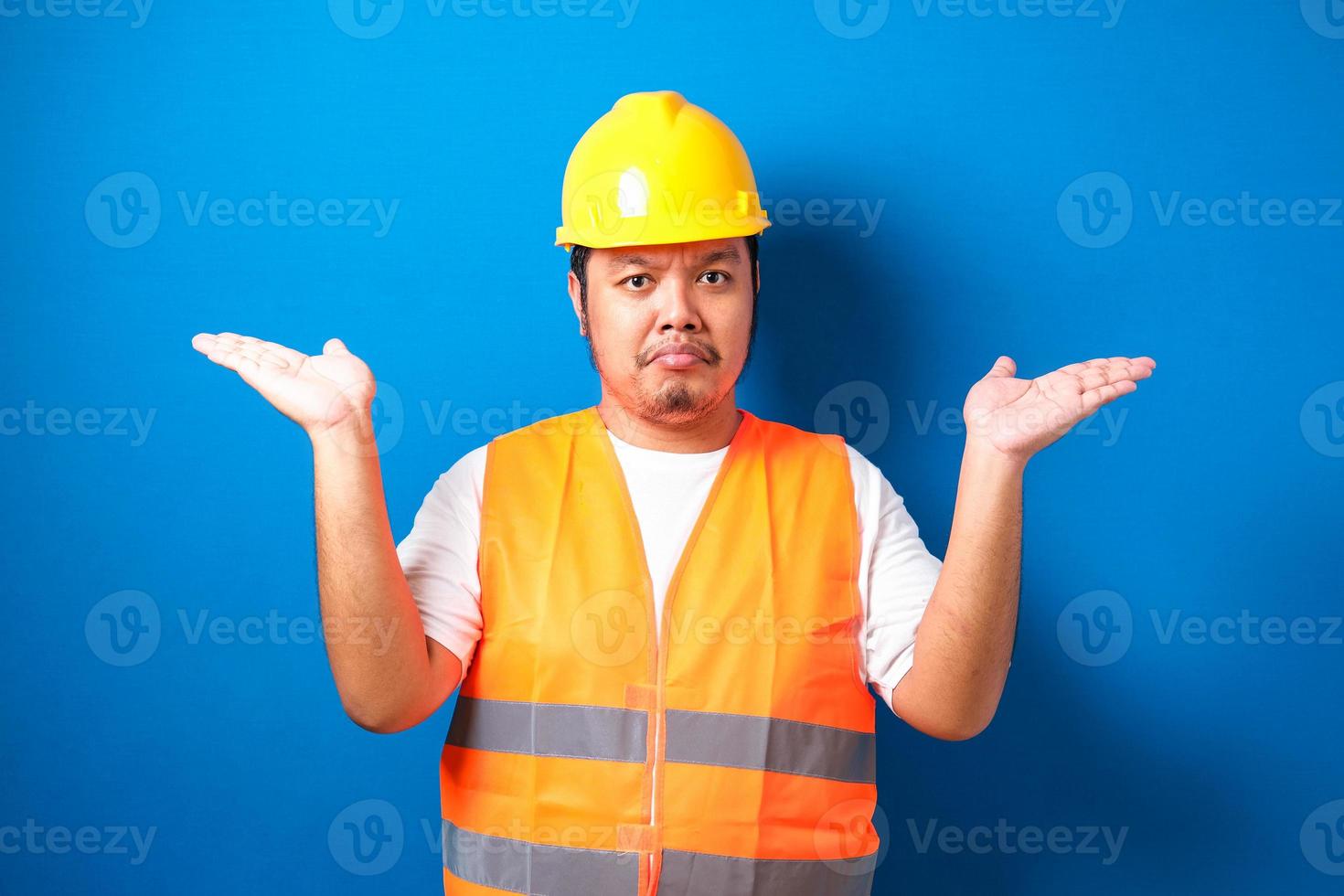 Young handsome fat asian worker man wearing orange safety vest uniform and helmet clueless and confused expression photo