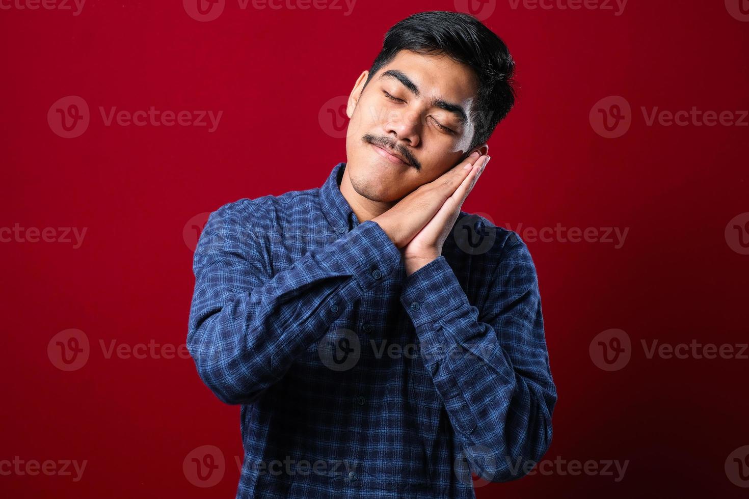 Asian handsome man wearing shirt sleeping tired dreaming and posing with hands together while smiling with closed eyes photo