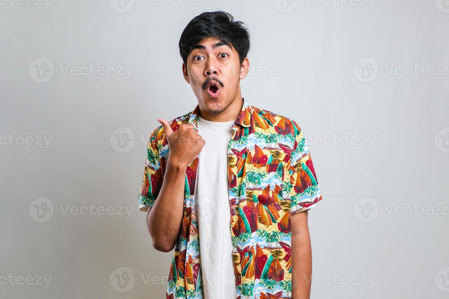 Asian man in white tshirt smiling and pointing to presenting something on his side, against red background with copy space photo