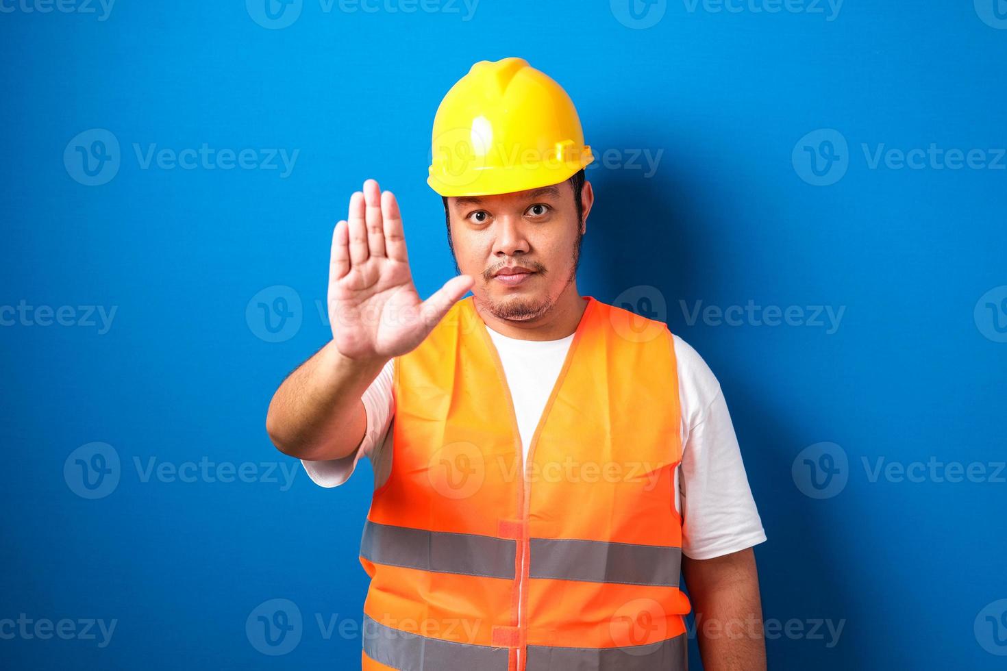 Fat asian workman wearing orange safety vest and yellow helmet making stop gesture photo