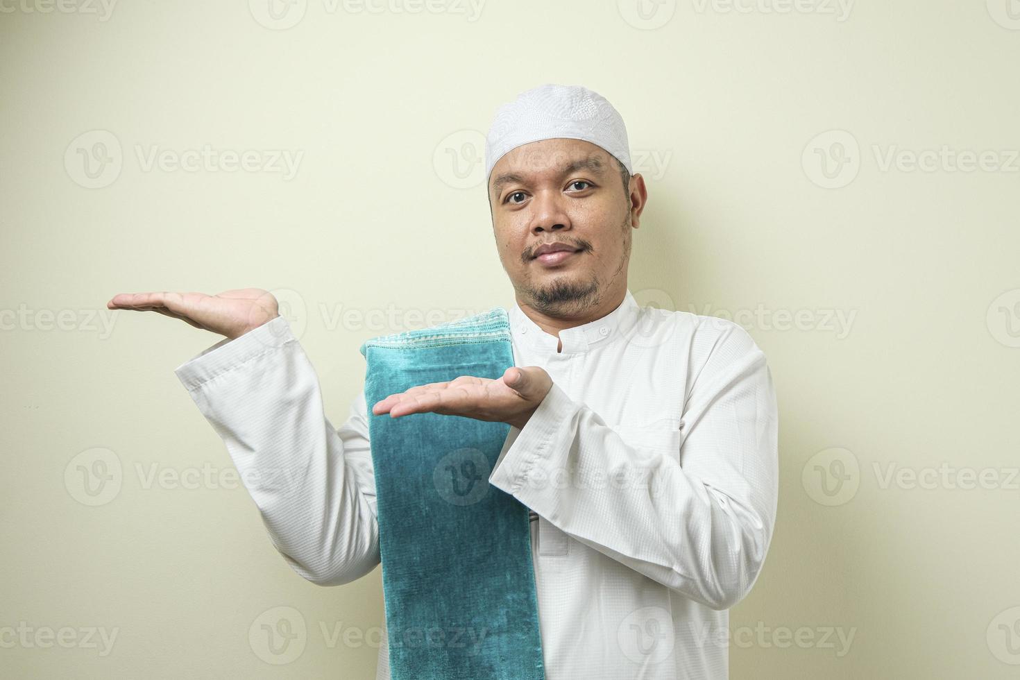 Portrait of Asian young muslim man smiling and pointing to presenting something on his side photo