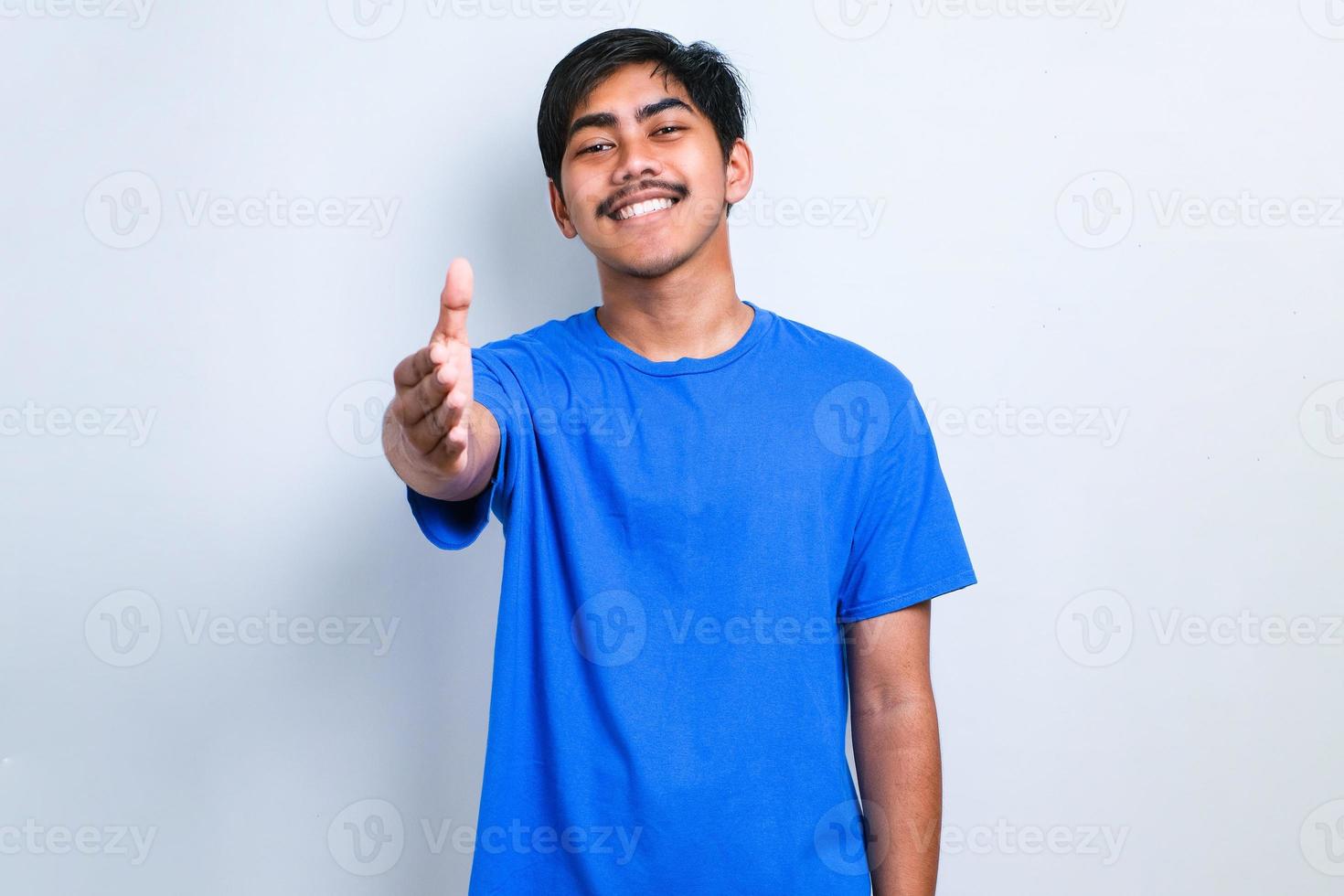 Asian young man wearing casual clothes smiling friendly offering handshake as greeting and welcoming photo