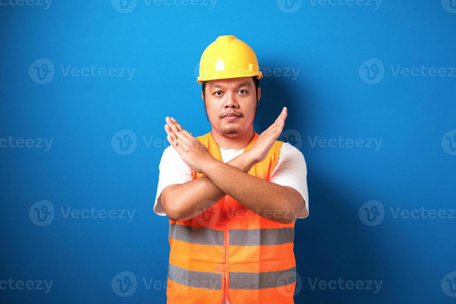 Fat asian workman wearing orange safety vest and yellow helmet making stop gesture photo