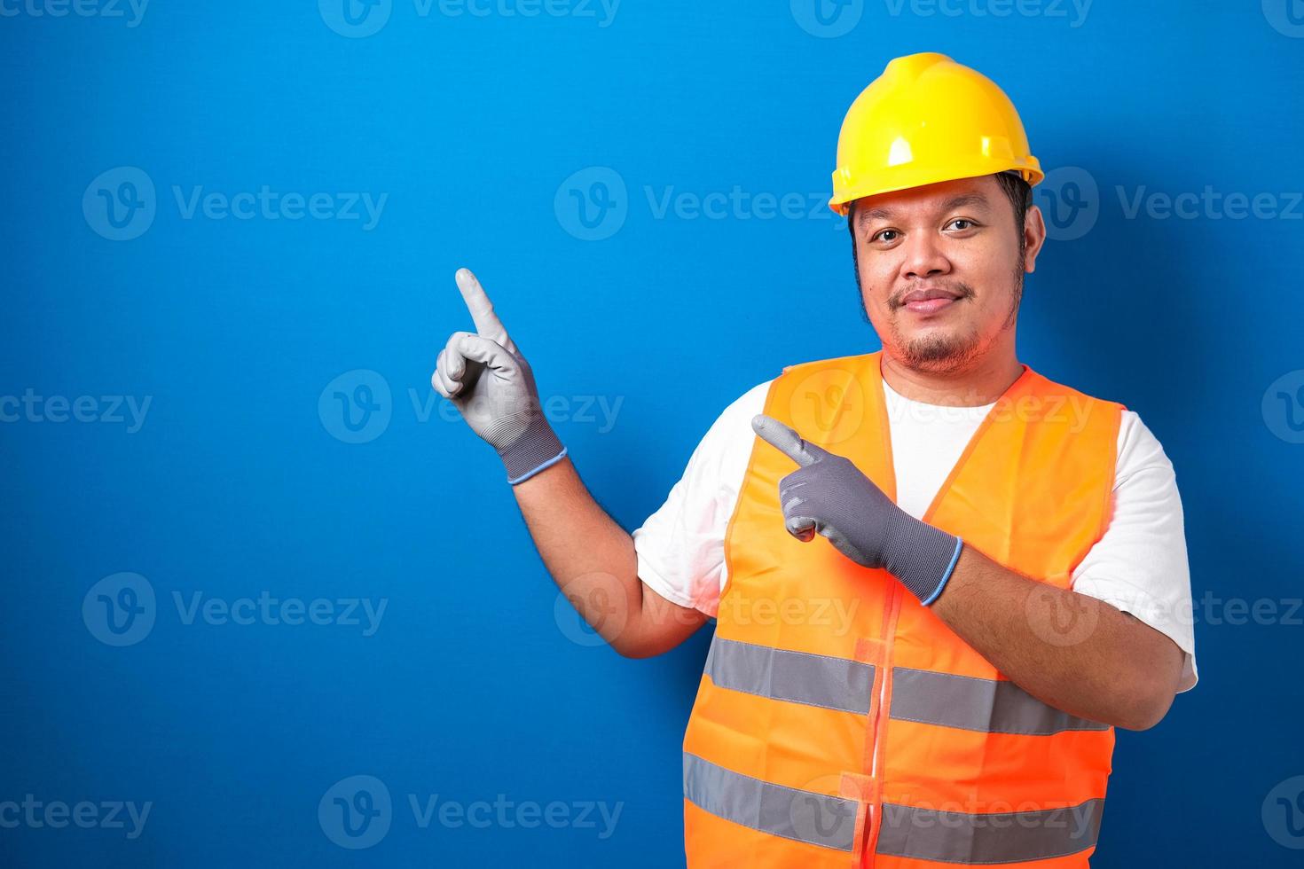 Fat Asian worker wearing a helmet presents something in his hand while facing sideways photo