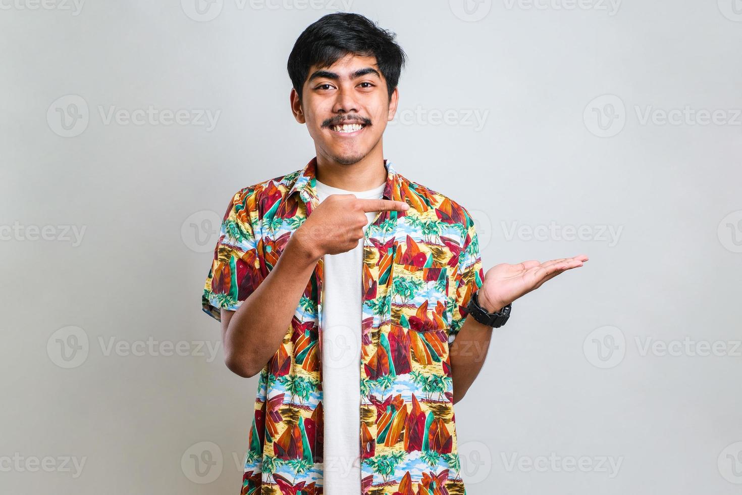 asian man with a big smile on face, pointing with hand finger to the side looking at the camera. photo