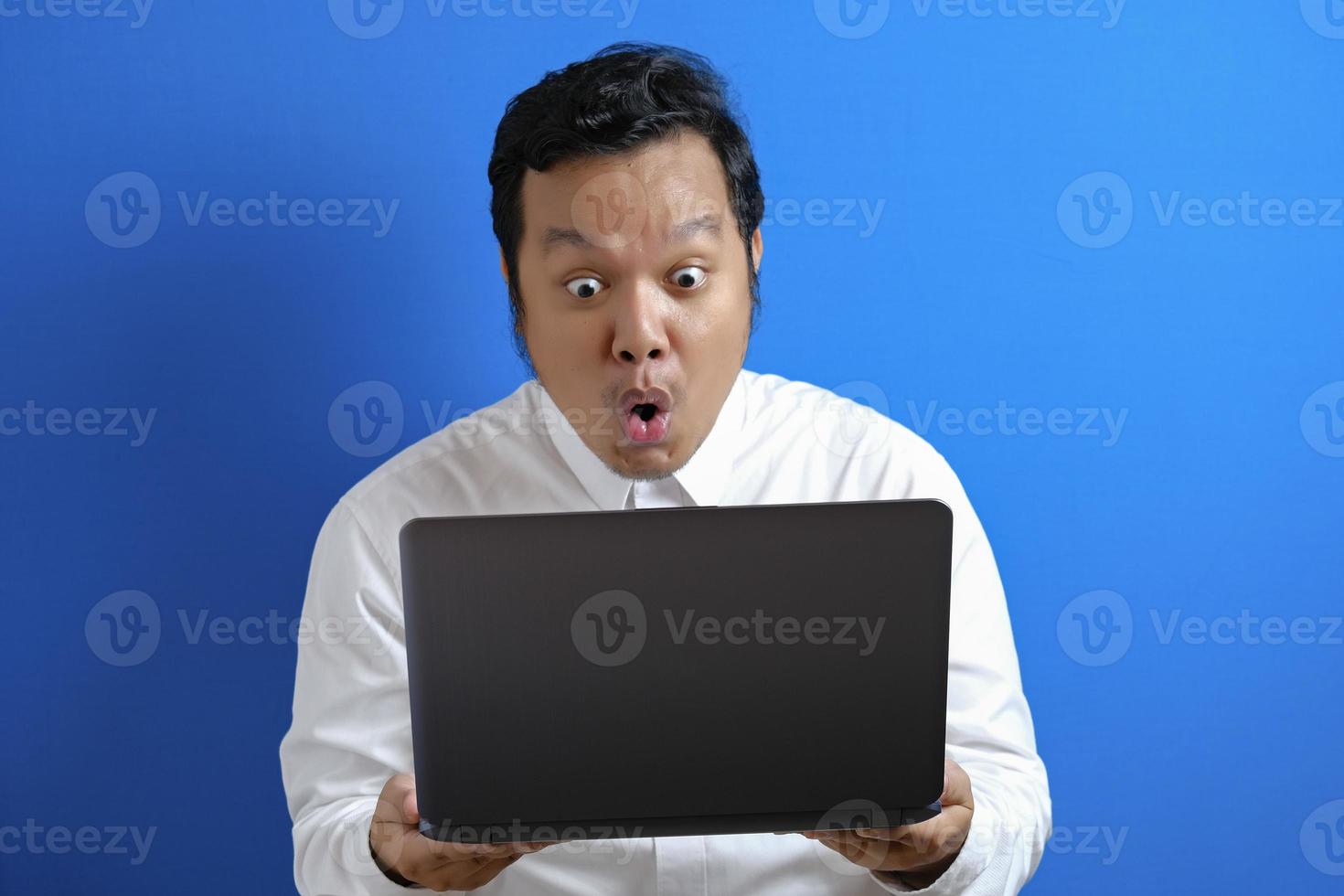 Young Asian businessman wearing casual white shirt looking at laptop, surprised expression. photo