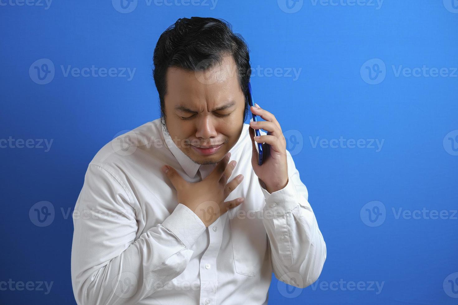 a photo of an asian man in an office worker looking sad over the news he received on his smart phone