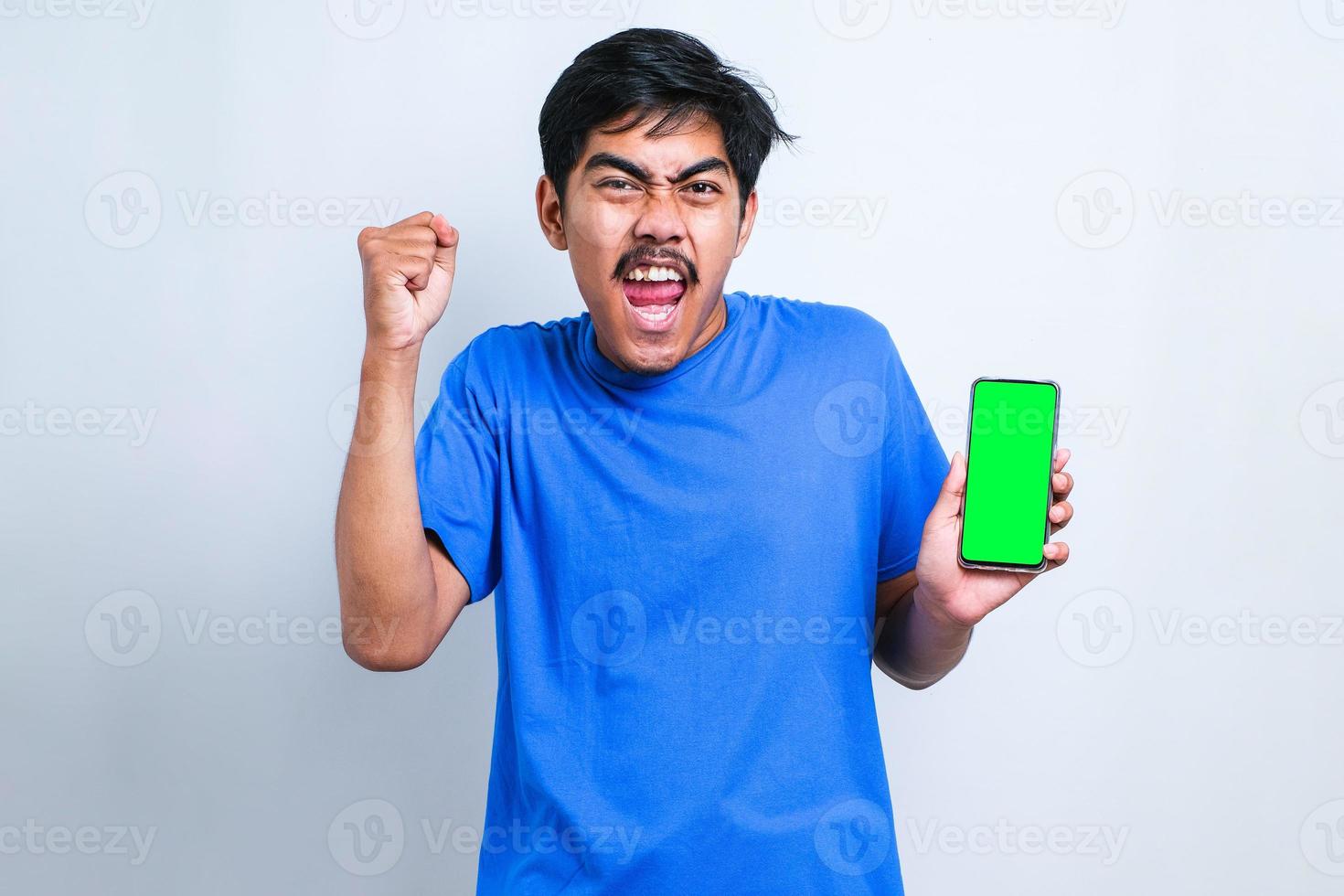 joven asiático usando un teléfono inteligente gritando orgulloso y celebrando la victoria y el éxito muy emocionado, animando la emoción foto