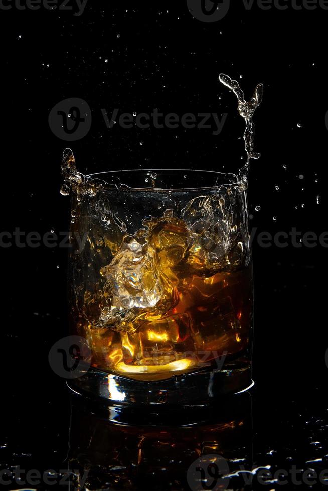 vaso de whisky escocés con salpicaduras y hielo sobre fondo negro foto