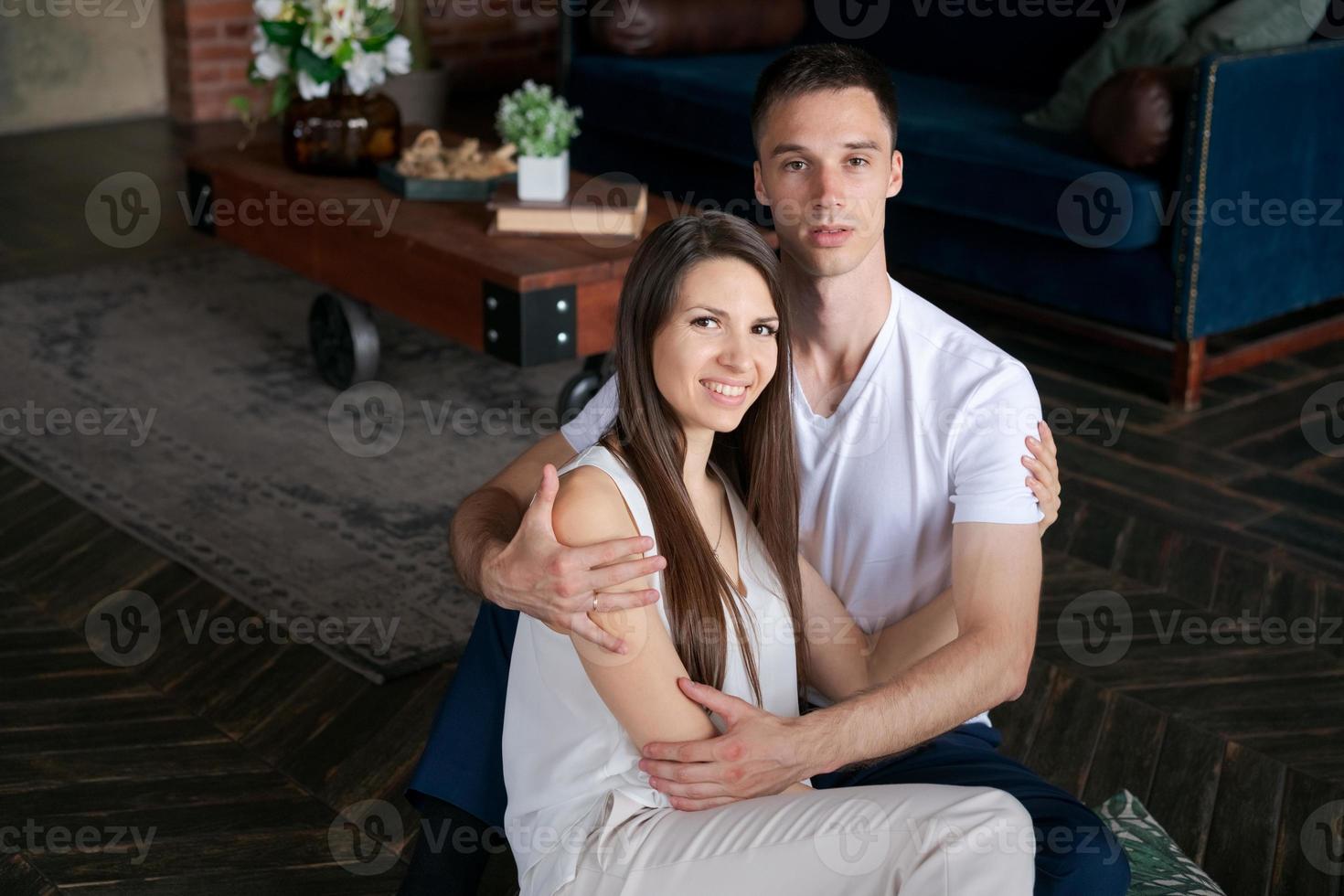 Smiling sincere young married couple hugging while sitting on warm heated floor photo