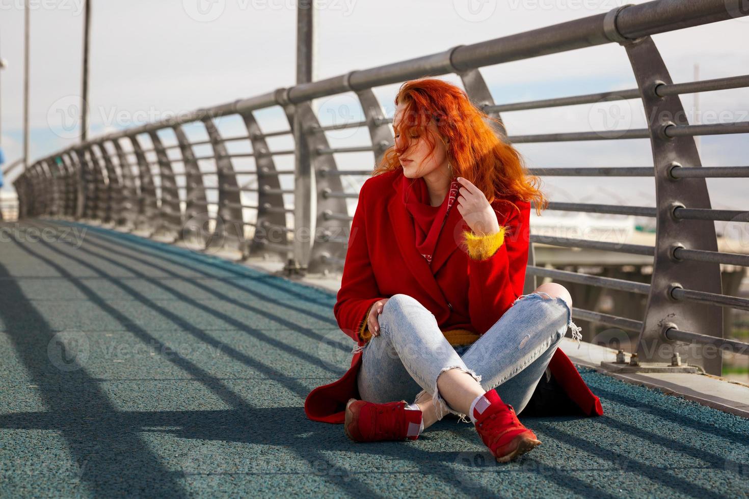 mujer con el pelo y un abrigo rojo sienta en un puente 5883702 Foto stock en Vecteezy