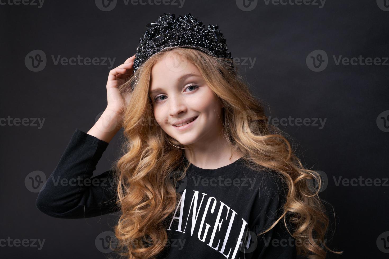 Adorable happy smiling little girl in princess crown celebrating on black photo