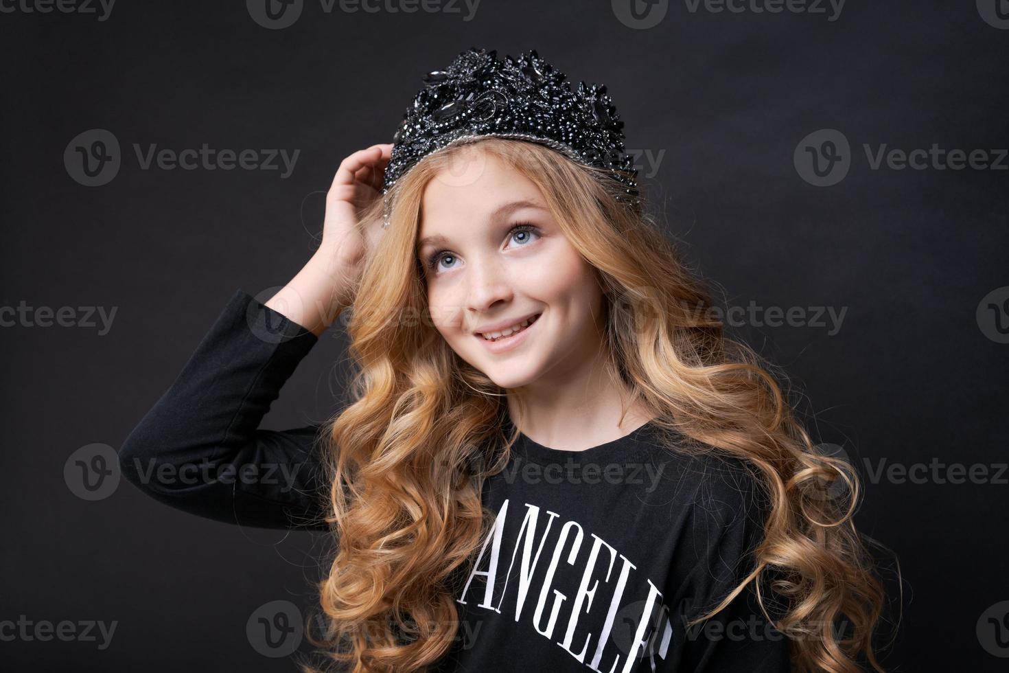 Beautiful little princess girl in black clothes with a crown on her head posing photo