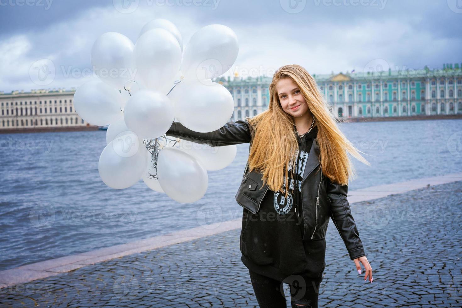 Caucasian girl holding white balloons standing by the river on the embankment photo