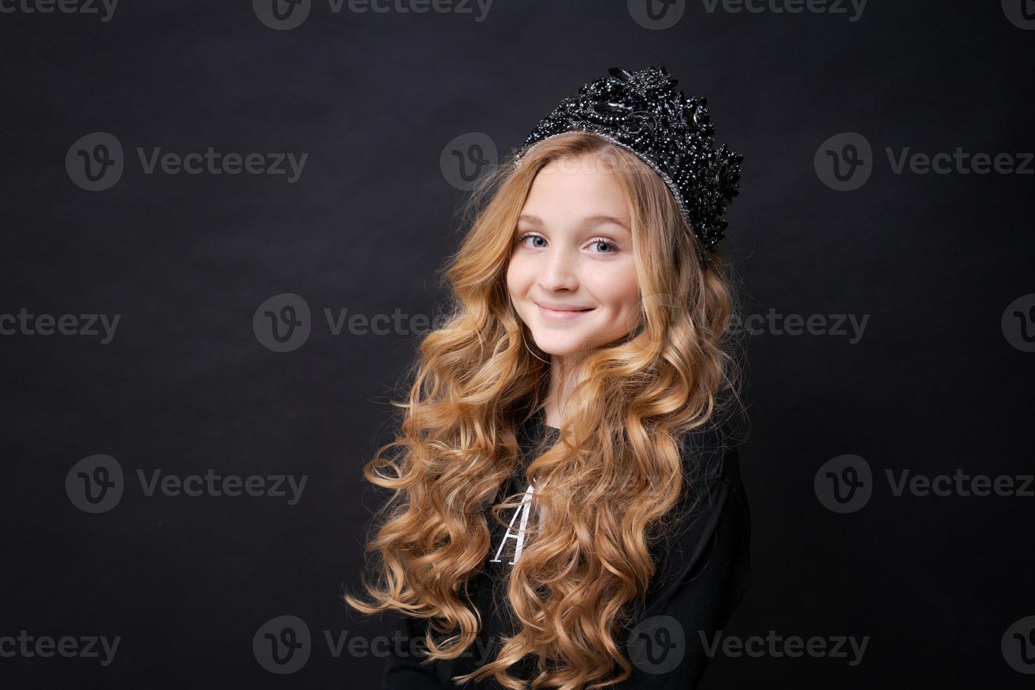 Adorable happy smiling little girl in princess crown celebrating on black photo