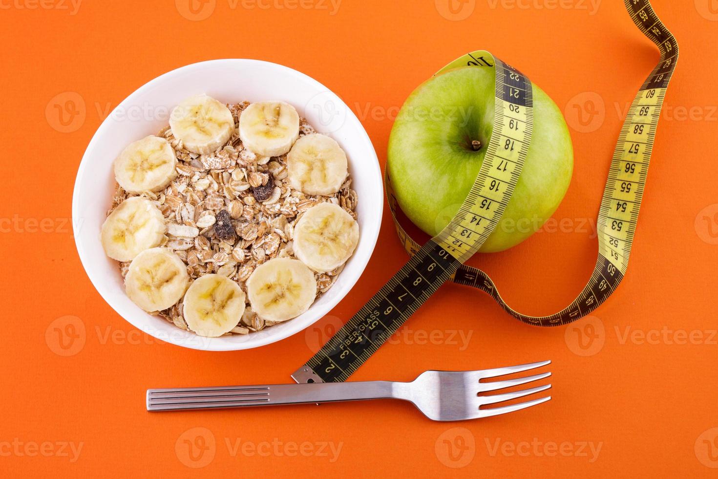 muesli with banana on orange background with apple and measuring tape photo