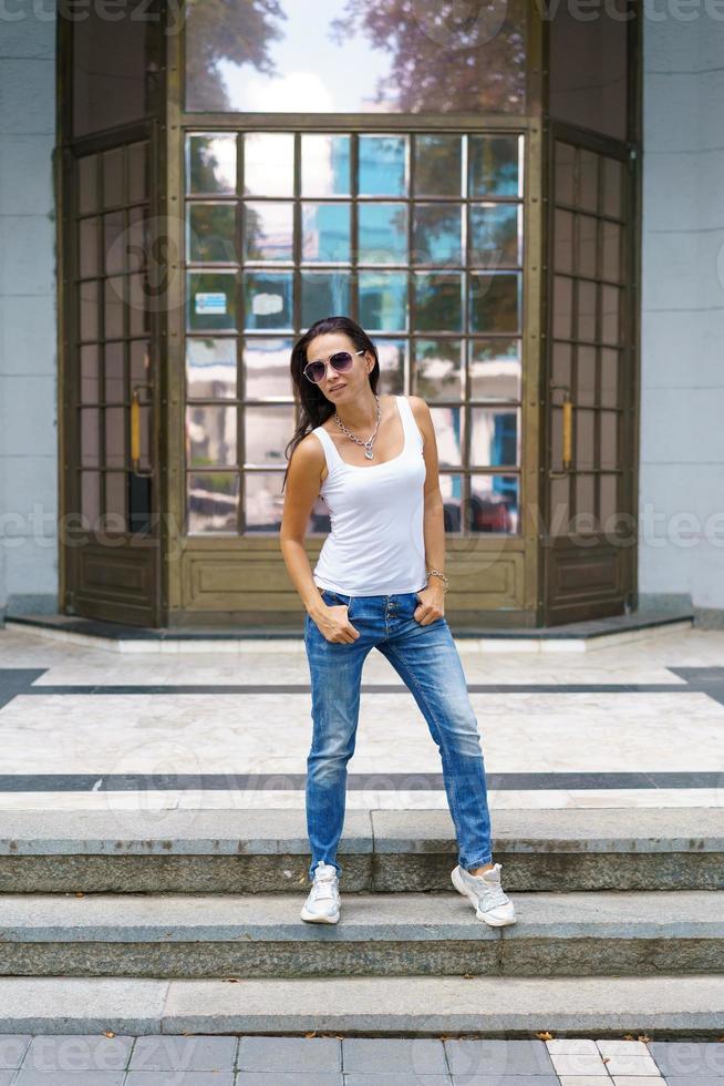 Cute woman in sunglasses poses on the steps in the street near the building photo